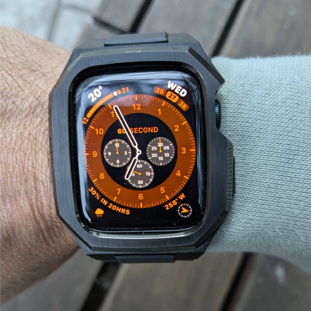 Apple watch in a black tactical band with a detailed display on a wrist, with a wooden surface for background