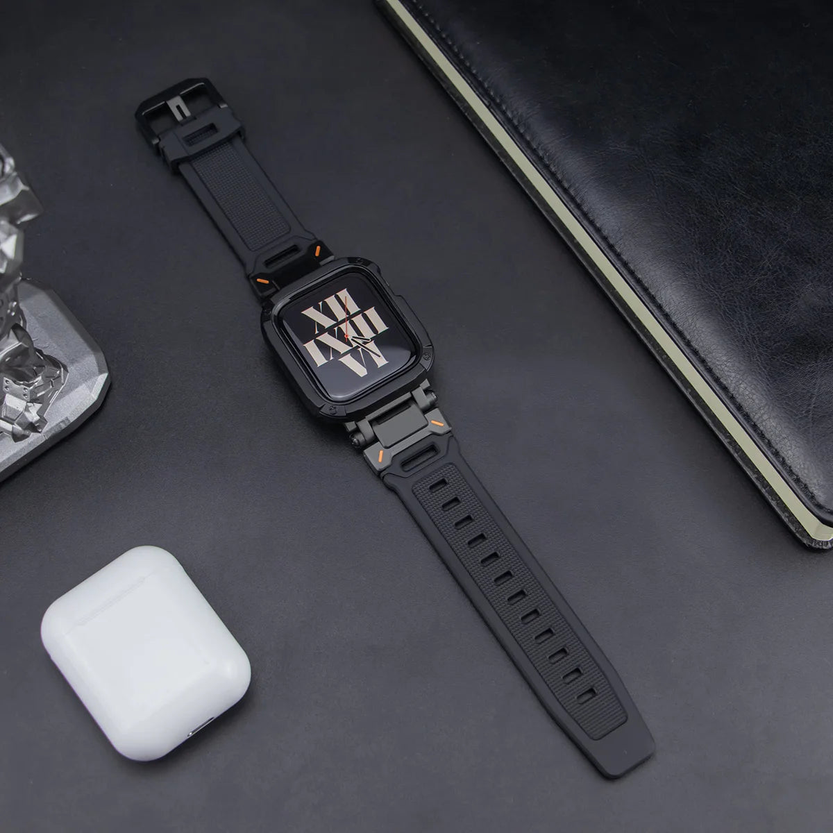 black apple watch band and case, layed down on a black table next to air pods and a black notebook