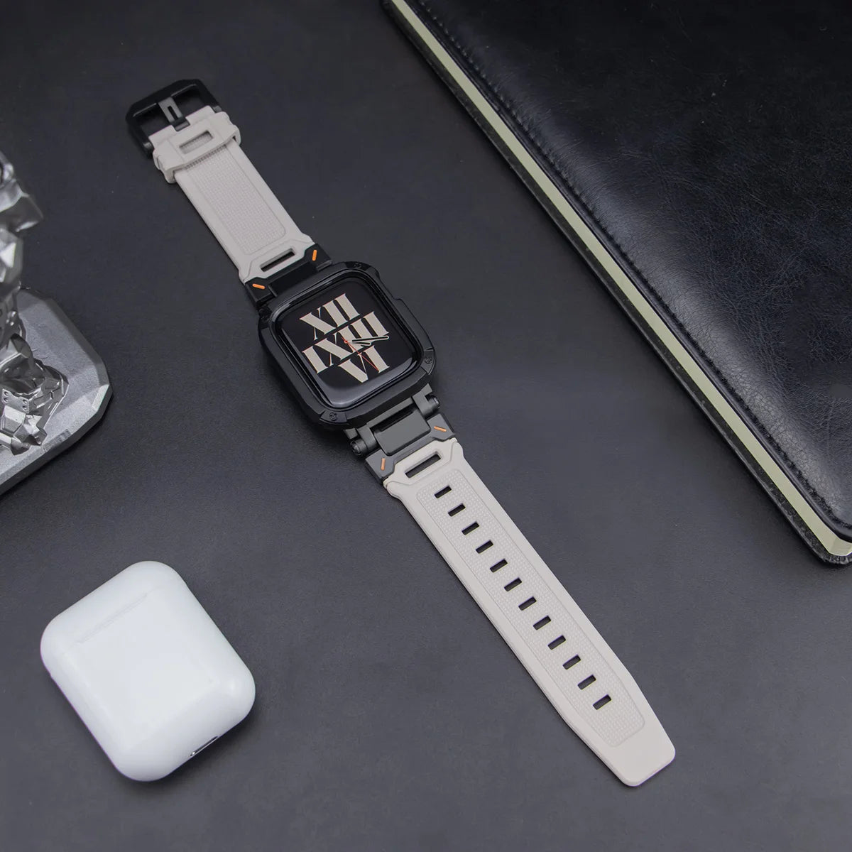 white apple watch band and black case, layed down on a black table next to air pods and a black notebook